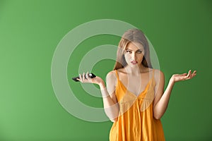 Emotional young woman with remote control on color background