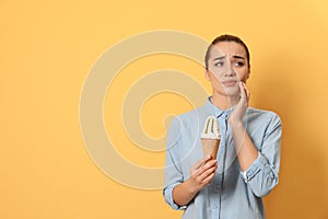 Emotional young woman with sensitive teeth and ice cream on color background.