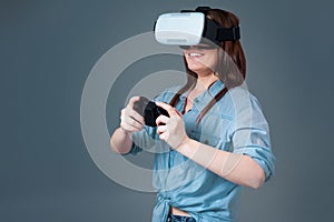 Emotional young woman using a VR headset and experiencing virtual reality on grey background
