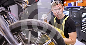 Emotionally pensive auto mechanic holds wrench and stares in surprise at motorcycle in service center 4k movie