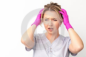 The emotionally shocked young female medical worker holding hands on her head fell into panic on white background