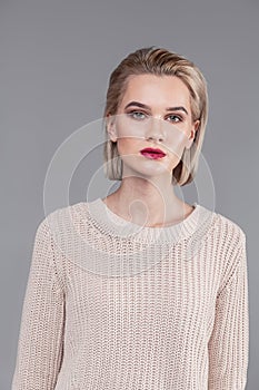 Emotionless blonde young girl wearing beige knitted sweater