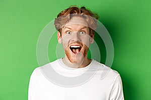 Emotions and fashion concept. Close up of surprised redhead man hear amazing news, staring at camera joyful, standing