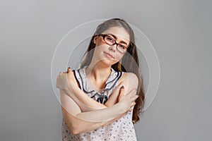 Emotions and people. Young brunette woman in glasses and blouse, hugging herself by the shoulders. Emotion of calm