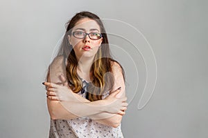 Emotions and people. Young brunette woman in glasses and blouse, hugging herself by the shoulders. Emotion of uncertainty