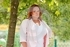 Emotions. Portrait of a plus-size woman showing her frustration and discontent. In the background green foliage of trees
