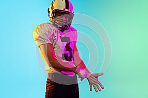 Portrait of one American football player in sports equipment helmet and gloves isolated on blue studio background in