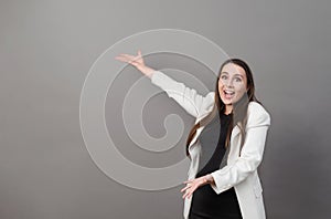 Emotions, young woman with long hair in a white jacket waves her hands and is surprised at the gray