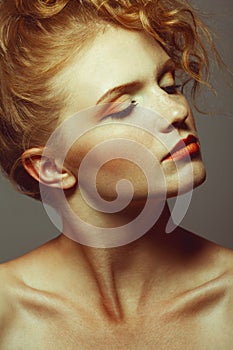 Emotive portrait of fashionable model with red ginger curly hair and evening make-up posing over grey background. Perfect skin