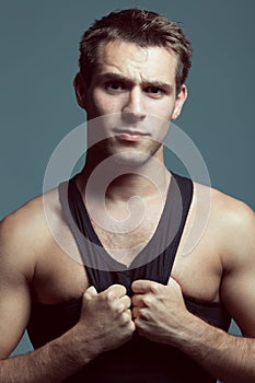 Emotive portrait of handsome boy with perfect body in black sleeveless shirt posing over gray background.  Look of verjuice. Close