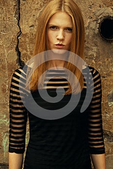 Emotive portrait of a young beautiful red-haired girl wearing trendy black cocktail dress, giving air kiss and posing over cracked