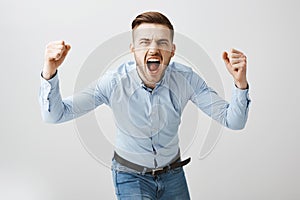 Emotive thrilled concerned european male boss in formal blue shirt and jeans bending towards camera yelling and raising photo