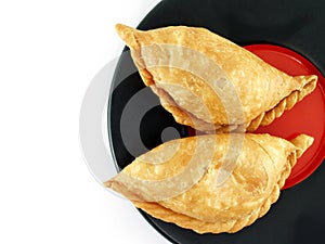 empanada, two latin america pastry on black and red ceramic plate isolated on white background