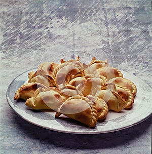 Empanadas, tanty, traditional Argentinian baked goods in a gray earthenware plate on a cloth background of the same color photo