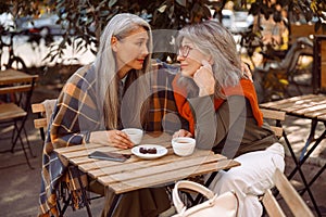 Empathic grey haired Asian woman hugs friend to cheer up at table in street cafe photo