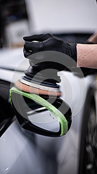 Employee of a car detailing studio or a car wash polishes the paintwork of a black car