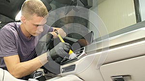 A employee of a car wash washes the car inside, he wipes the instrument panel with a special brush.