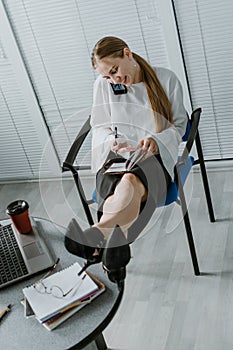 Employee care. Relaxed happy young business woman entrepreneur put legs on table, talking on cell phone, drinking coffee