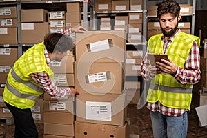 Employee checking stock and inventory with tablet computer in retail warehouse full of goods. Male workers working in