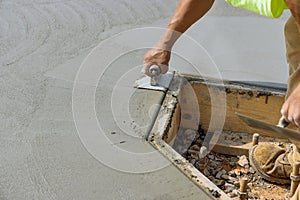 An employee of a construction company uses a stainless steel edger to form a corner in the new cement floor using wet