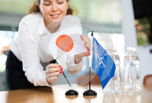 Employee of delegation prepares negotiating table - sets up flag of NATO (OTAN) and Japan