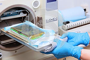An employee of the dental clinic takes out sterilized instruments. Cabinet for high-temperature processing of medical or dental