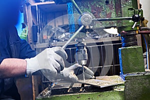 Employee drilling aluminium flat steel plate with bench drill. Metal Drill bit makes holes in Steel billet on industrial machine.