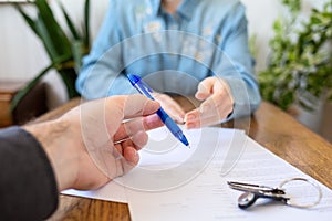 An employee gives the client a pen to fill out documents. Hands close-up. There are papers and keys on the table. Rental and