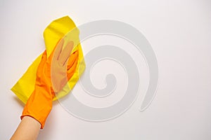 Employee hand in orange rubber protective glove wiping white wall from dust with yellow dry rag. General or regular cleanup.