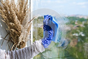 Employee hand in rubber protective glove with micro fiber cloth wiping window from dust. General spring cleaning