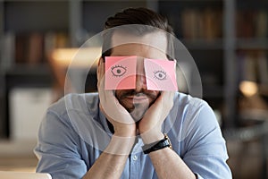 Employee hides eyes with sticky notes wants sleep at workplace
