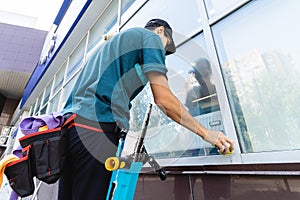 An employee of a professional cleaning service in overalls washes the facade and windows with special devices