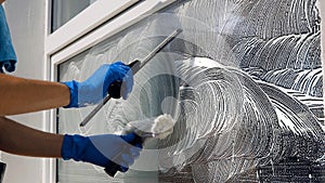 An employee of a professional cleaning service in overalls washes the glass of the windows of the facade of the building