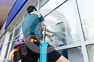 An employee of a professional cleaning service in overalls washes the glass of the windows of the facade of the building