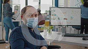 Employee with protection mask sitting on wheelchair in front of camera