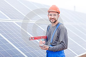 A employee of the solar cell station, stands with a waterpasand writes something in a notebook.