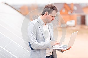 An employee of the solar station holds a laptop, standing next to the solar panel.