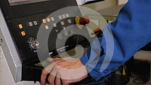 The employee stands at the control panel of the machine with numerical control. It controls the process of a computer mouse and bu