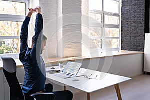 Employee Stretching At Office Desk