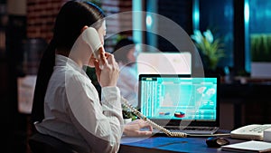 Employee taking landline telephone call while working with financial graphs