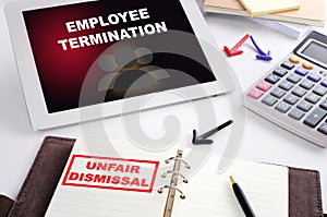 Employee termination words on computer tablet and unfair dismissal stamp on notebook on busy working desk