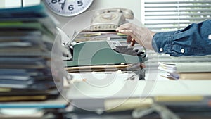 Employee typing with a typewriter and piles of paperwork