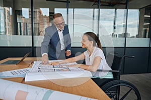 Employee in a wheelchair works in the office on drawings