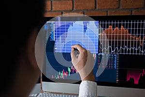 Employees analyze the graph of the stock market using a pen pointing to the computer screen