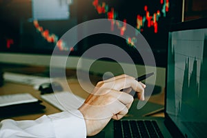 Employees analyze the graph of the stock market using a pen pointing to the computer screen