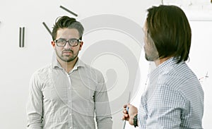 Employees discuss business plans. Highlighted focus on serious Caucasian man looking at camera while standing against