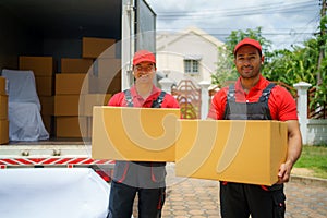 The employees of the House Removals company are standing behind the truck with boxes and smiling