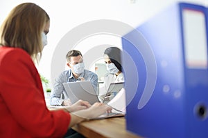 Employees in office are sitting at table wearing protective medical masks