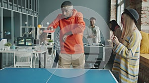 Employees playing table tennis having fun enjoying work break in modern office