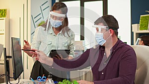 Employees with protection masks discussing looking at computer